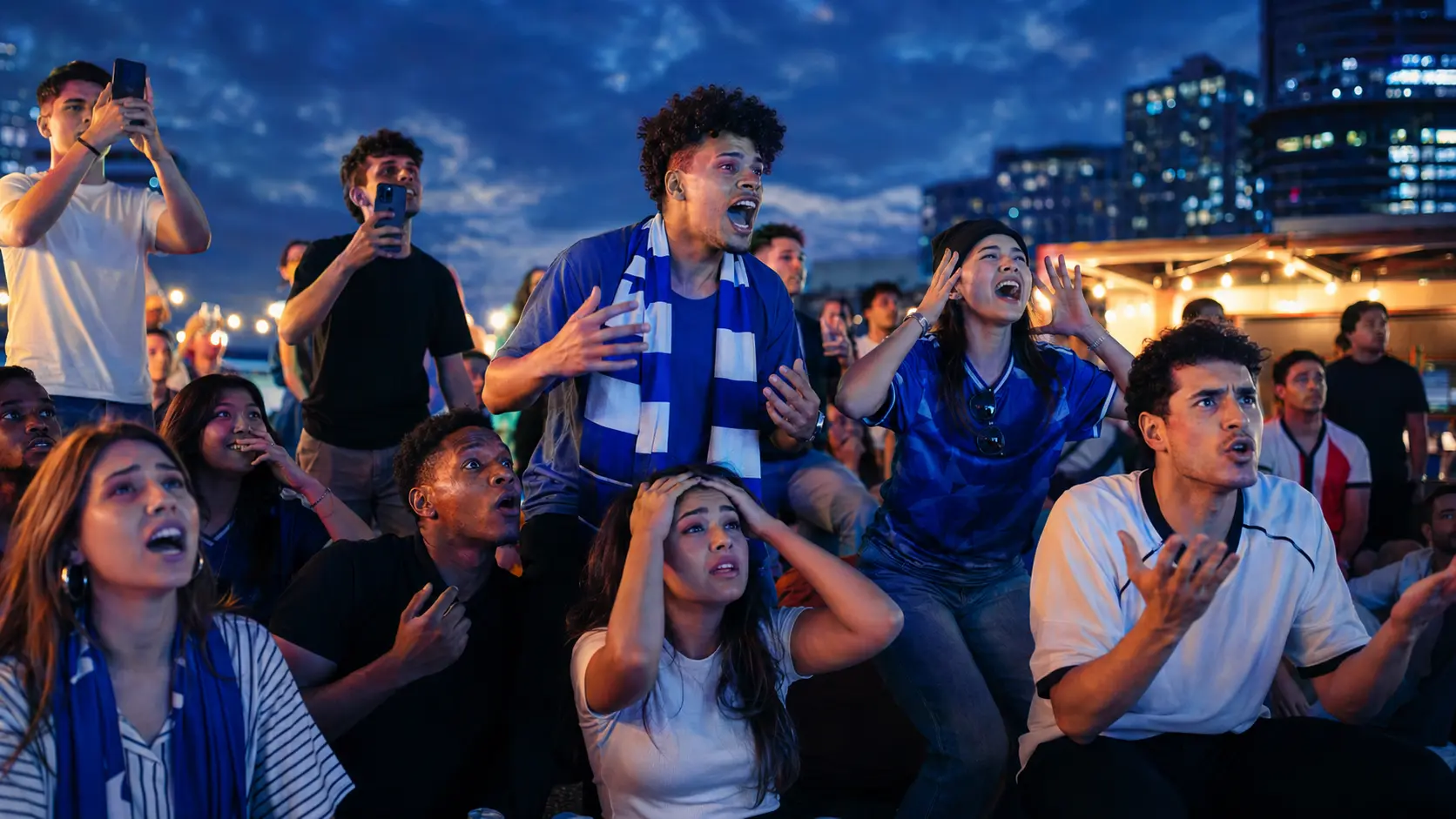 A diverse group of young football supporters reacting together at an outdoor city watch party.